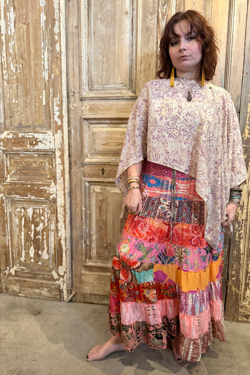 Woman wearing a colorful patchwork skirt and patterned top in front of a wooden door.